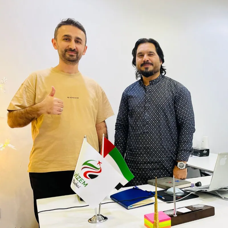 Vizem Dubai ekibinden iki kişi ofiste, önlerinde Vizem Dubai masa bayrağı